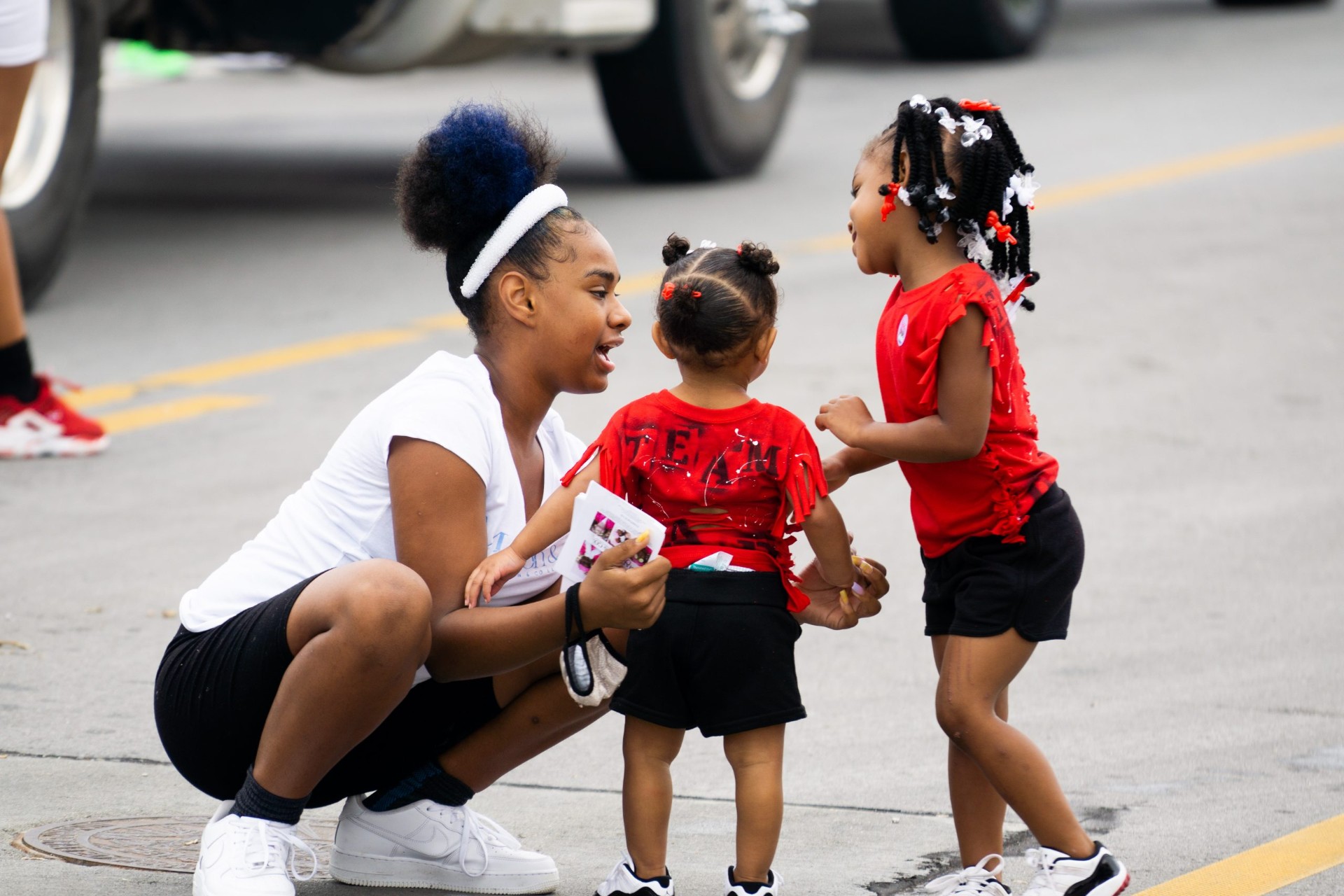 A young woman kneeling to talk with two toddlers in red