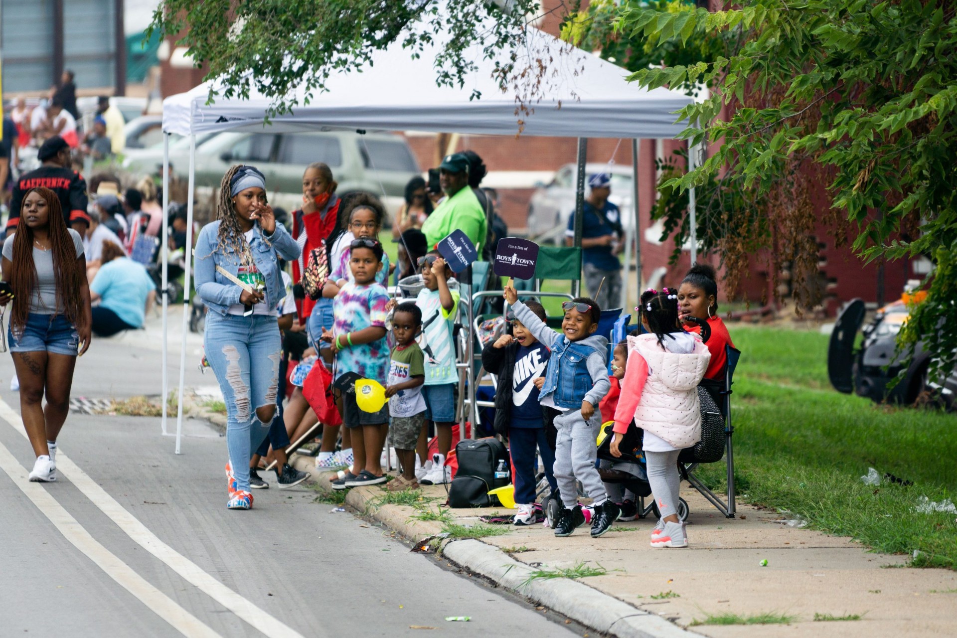 Families cheering from the sidewalk under a shade tent